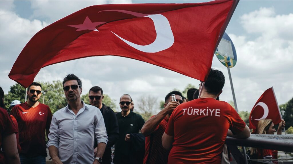 Gaziler Günü anlamı haberi için temsili görsel: bulutlu gökyüzü altında büyük bir Türk bayrağı taşıyan kalabalık (Gaziler Günü haberi, temsili görsel)