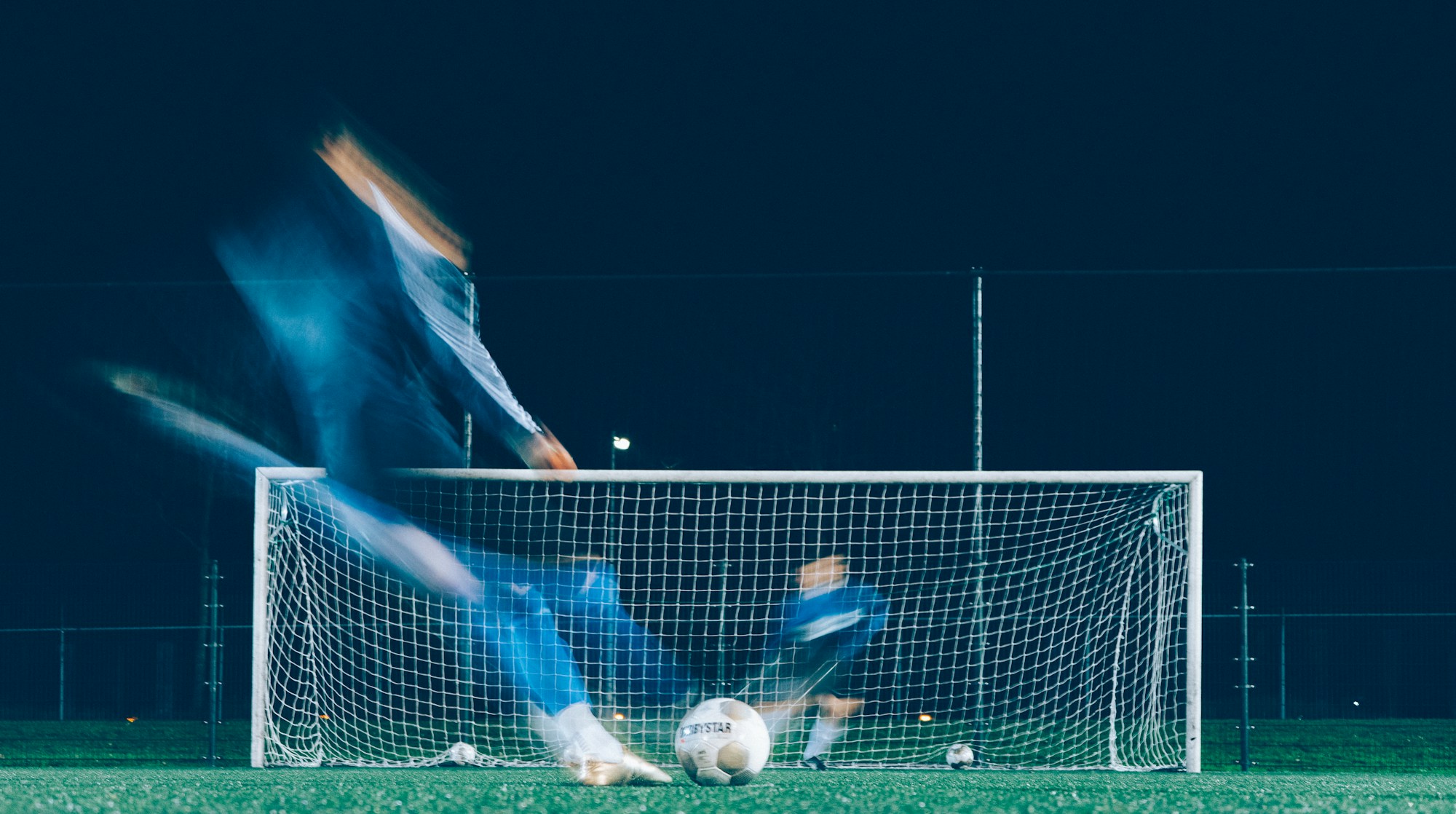 Gece ışıklandırmasında kaleye şut çeken bir futbolcu, hareket bulanıklığıyla (temsilî)