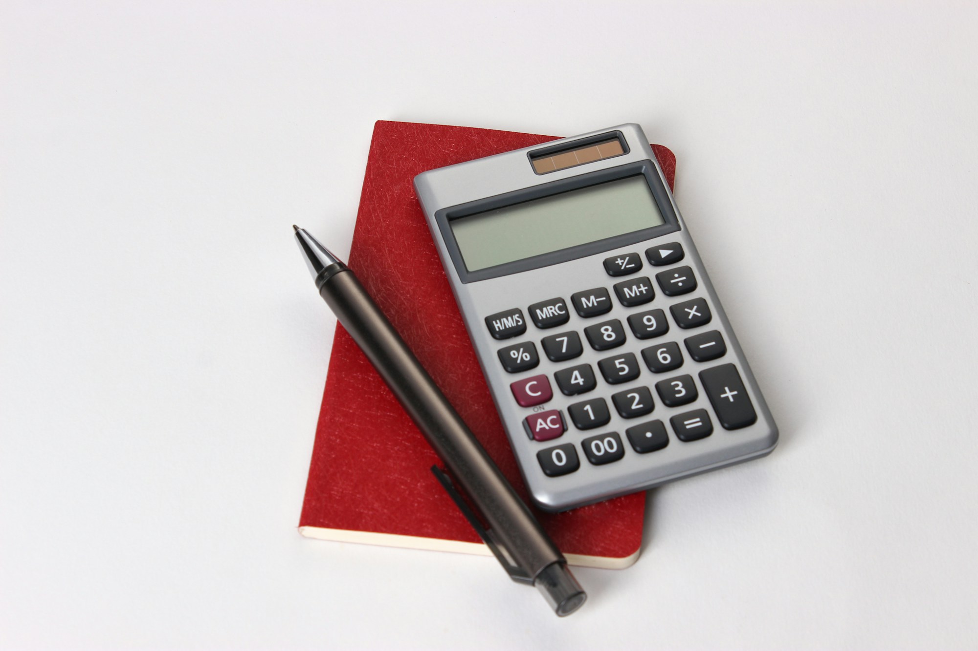 Kırmızı defter üzerinde bir hesap makinesi ve kalem